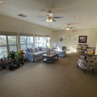 A spacious and well-lit living room with comfortable seating, large windows, and ceiling fans.