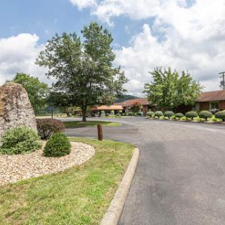 A scenic view of a landscaped entrance to a building along a winding road, surrounded by trees and clouds.