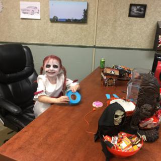 A child in Halloween costume enjoying treats at an office desk.