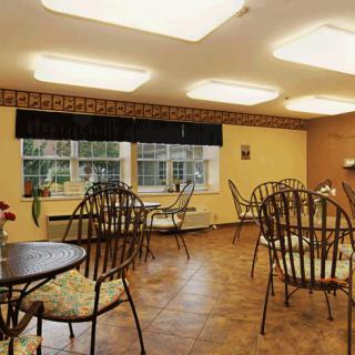 A cozy dining room with multiple tables and chairs, featuring large windows and a wooden floor.
