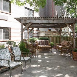 A cozy outdoor patio with chairs and a wooden gazebo, surrounded by plants.