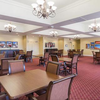 A spacious dining area with multiple tables and chairs, featuring elegant chandeliers and a carpeted floor.