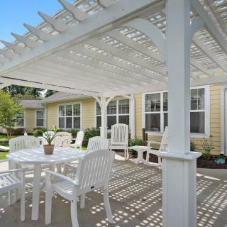 A sunny backyard patio with a white pergola and outdoor furniture.