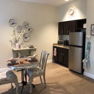 A cozy kitchen and dining area featuring a small table with chairs, a refrigerator, and decorative elements.