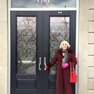 A woman in a burgundy coat stands in front of ornate double doors.