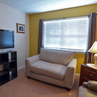 A cozy living room with a sofa, television, and window with blinds.