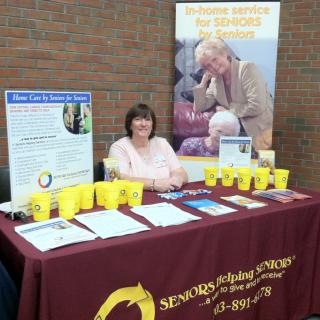 A representative staffing an informational booth for senior care services at a community event.