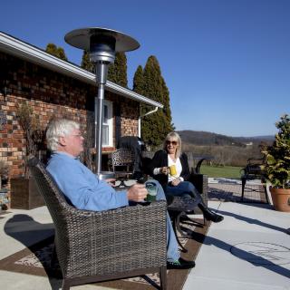 Two people enjoying a conversation on a sunny patio overlooking a scenic landscape.