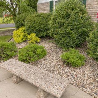 A stone bench in a landscaped garden with shrubs and pebbles.