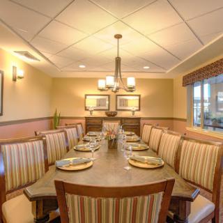 A stylish dining room featuring a long table and striped seating, illuminated by elegant lighting.