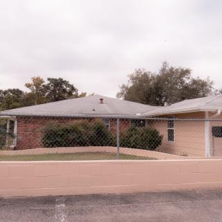 A suburban residential house with a brick wall and driveway on a cloudy day.