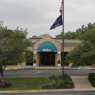 A building entrance with a green awning and flags, surrounded by trees.