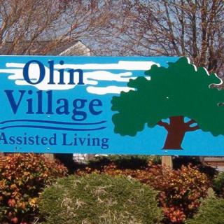 A sign for Olin Village Assisted Living with a tree graphic.