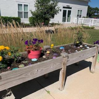 A vibrant flower garden in a wooden planter, showcasing colorful blooms and decorative stones.