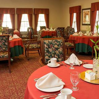 An elegantly set dining room with tables covered in red tablecloths and neatly arranged chairs.