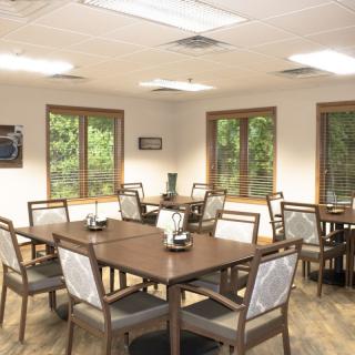 An empty dining area with several tables and chairs, lit by overhead lights and natural light from the windows.