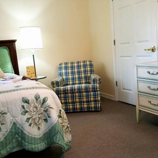 A cozy bedroom with a bed, plaid armchair, and white dresser.