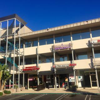 A modern shopping complex featuring various storefronts under a clear blue sky.