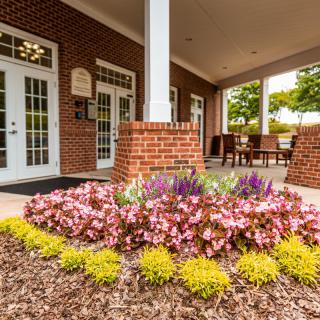 The entrance features a beautifully landscaped garden with blooming flowers in front of a brick building.