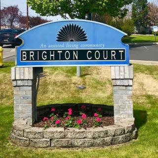 A community sign for Brighton Court, set against a backdrop of greenery and flowers.