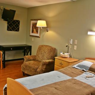 A hospital room featuring a bed, comfortable chair, desk, and medical equipment.