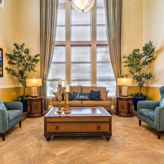 A luxurious living room featuring a central sofa, armchairs, and a wooden coffee table, complemented by tall windows and decorative plants.