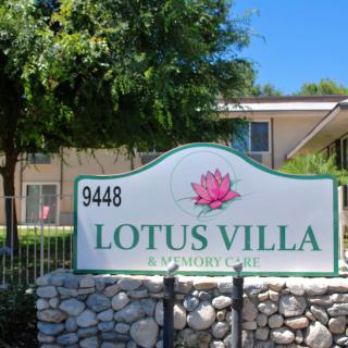 A sign for Lotus Villa in front of a residential building with trees and a stone base.