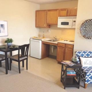 A cozy apartment with a small kitchen and dining area, featuring wooden cabinets, a microwave, refrigerator, and a table with chairs.