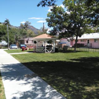 A sunny day view of a gazebo surrounded by grass, trees, and houses.