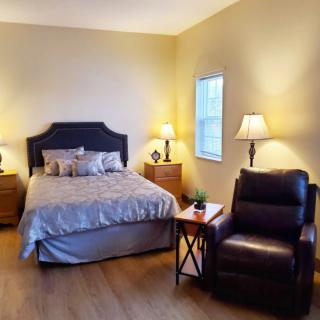 A cozy bedroom with a neatly made bed, accompanied by a comfortable chair and warm lighting from the lamps on the nightstands.
