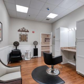 A neatly organized salon room with a chair, mirror, hair dryer, and bright lighting.