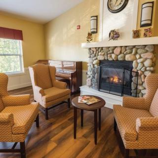 A cozy living room with a stone fireplace, surrounded by armchairs and wooden flooring.