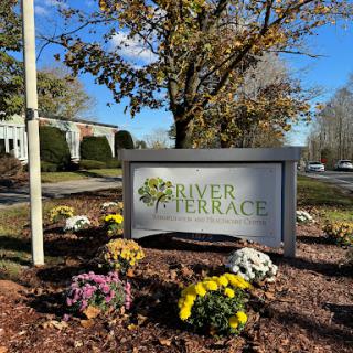 A welcoming sign for River Terrace, surrounded by colorful flowers and a clear blue sky.