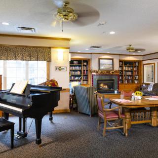 A cozy living room featuring a grand piano, fireplace, and bookshelves filled with books.