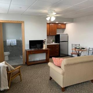 A cozy living space with a kitchenette, sofa, television, dining table, and an adjoining bathroom.