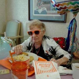 Elderly woman enjoying a meal at Whataburger with festive balloons in the background.