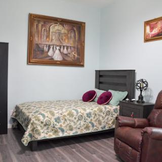 A cozy and well-decorated bedroom featuring a comfortable bed, a recliner chair, and artistic wall decorations.