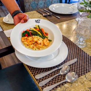 A bowl of pasta with shrimp and vegetables being served at a restaurant.