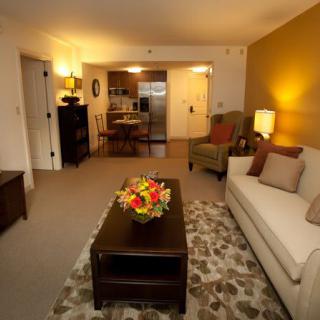 A cozy living room with modern decor, featuring a white sofa and a central coffee table adorned with flowers.