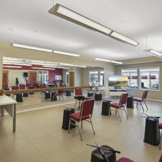A spacious dance studio with mirrors, chairs, and ample lighting.