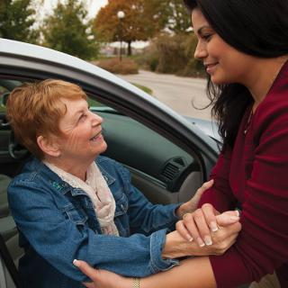 A young woman assists an elderly woman getting out of a car.