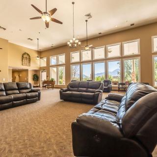 A spacious living room with multiple sofas, large windows, and ceiling fans.