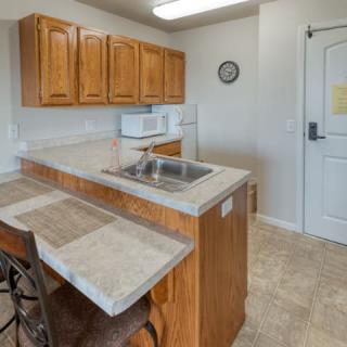 A small kitchen area with wooden cabinets and a countertop, featuring a microwave and sink.