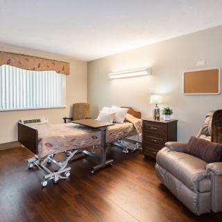 A well-furnished hospital room featuring a medical bed, recliner chair, and warm lighting.