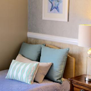 A cozy corner of a bedroom showcasing a neatly made bed with decorative pillows, accompanied by a bedside lamp and wall art.