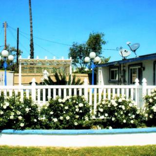 A white fence surrounds a garden with blooming flowers in front of a house.