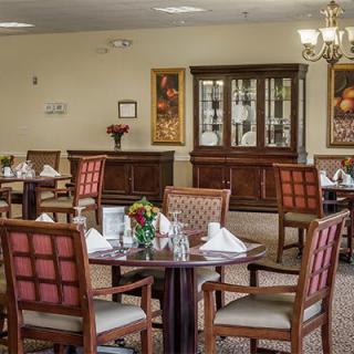 An elegantly decorated dining area with neatly arranged tables and chairs, featuring a chandelier and floral centerpieces.