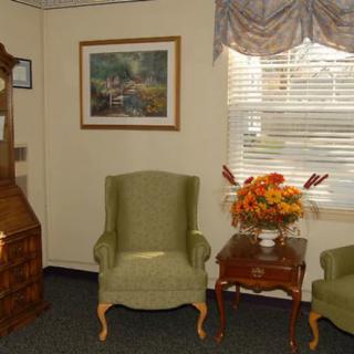 A cozy living room with green armchairs, a wooden table with a flower arrangement, and a painting on the wall.