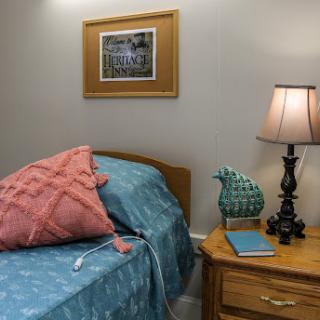 A cozy bedroom corner featuring a neatly made bed, decorative pillows, and a bedside lamp beside a wooden nightstand.