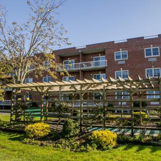 A garden with a pergola in front of a brick apartment building.